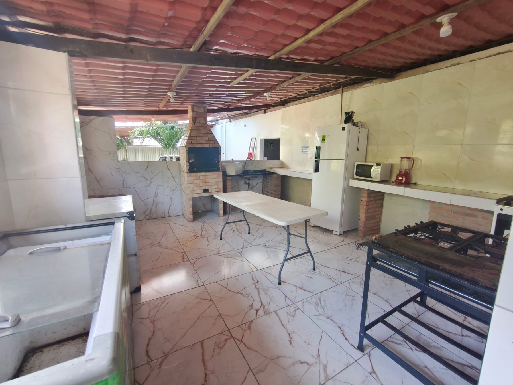Cozinha do Studio29 com churrasqueira de tijolos, geladeira, freezer, fogão industrial, micro-ondas e bancadas de apoio