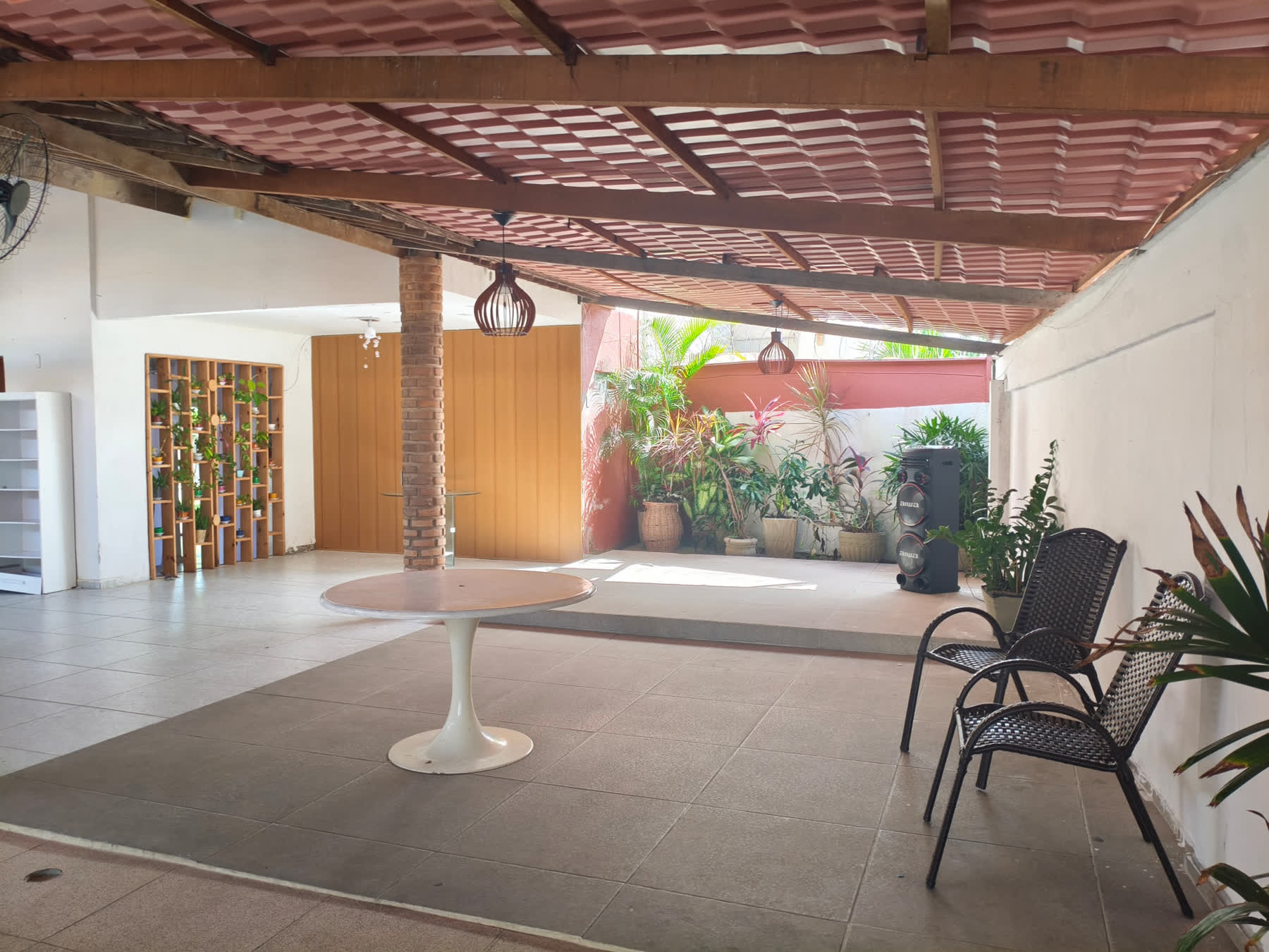 Pátio do Studio29 com mesa redonda branca, cadeiras de fibra e plantas ao fundo