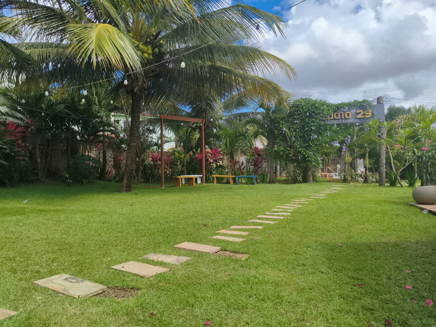 Caminho de pedras atravessando o gramado do Studio29 até as palmeiras e a placa do espaço